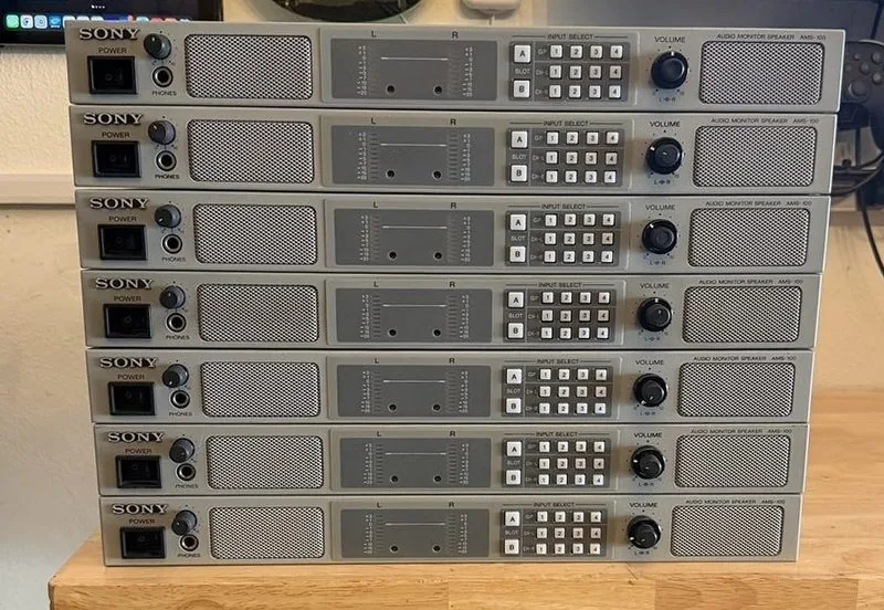 Seven Sony AMS-100 audio monitor speakers lined up on a wooden bench
