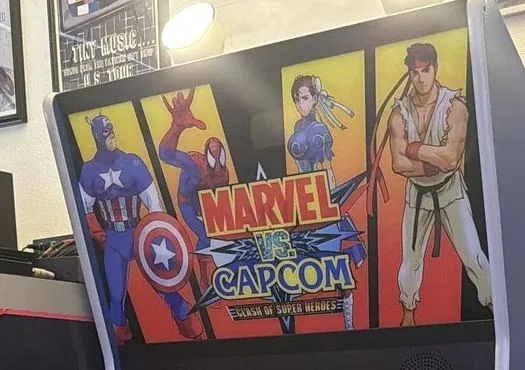 Close-up of the Marvel vs. Capcom marquee showing Captain America, Spider-Man, Chun-Li and Ryu, the machine switched off
