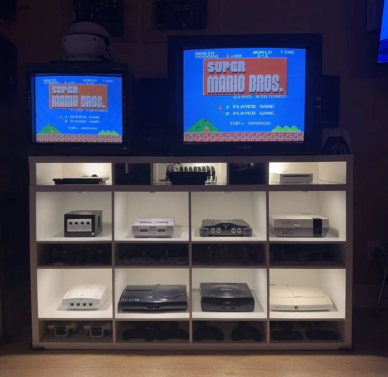 Lit display shelf of retro consoles at night with two Sony PVM monitors showing Super Mario Bros above