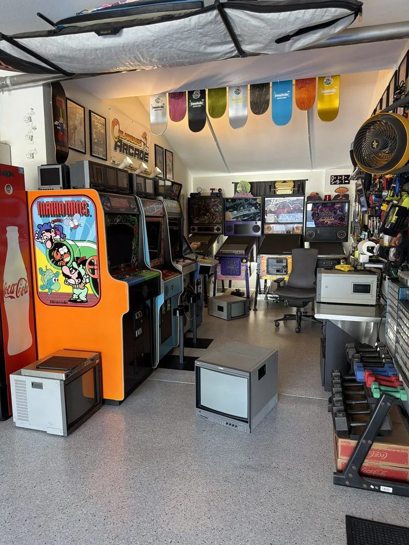 The garage arcade mid-project: cabinets, pro monitors on the floor, decks overhead, and work in progress everywhere