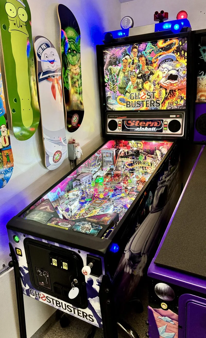 Stern Ghostbusters Premium pinball machine lit beside three skateboard decks hung on the wall