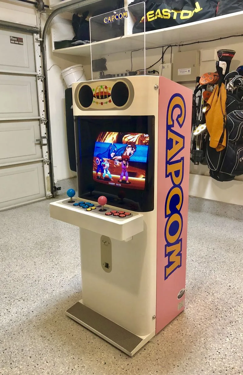 The pink Capcom Mini Cute unwrapped in the garage, running a Capcom fighter on its screen