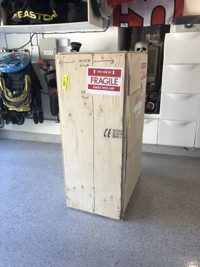Hand-built plywood shipping crate standing in the garage with FRAGILE labels and hand-written dimensions
