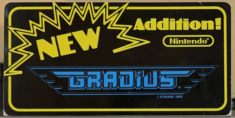 Original Nintendo PlayChoice-10 arcade topper for Gradius, the blue winged logo on black inside a yellow border