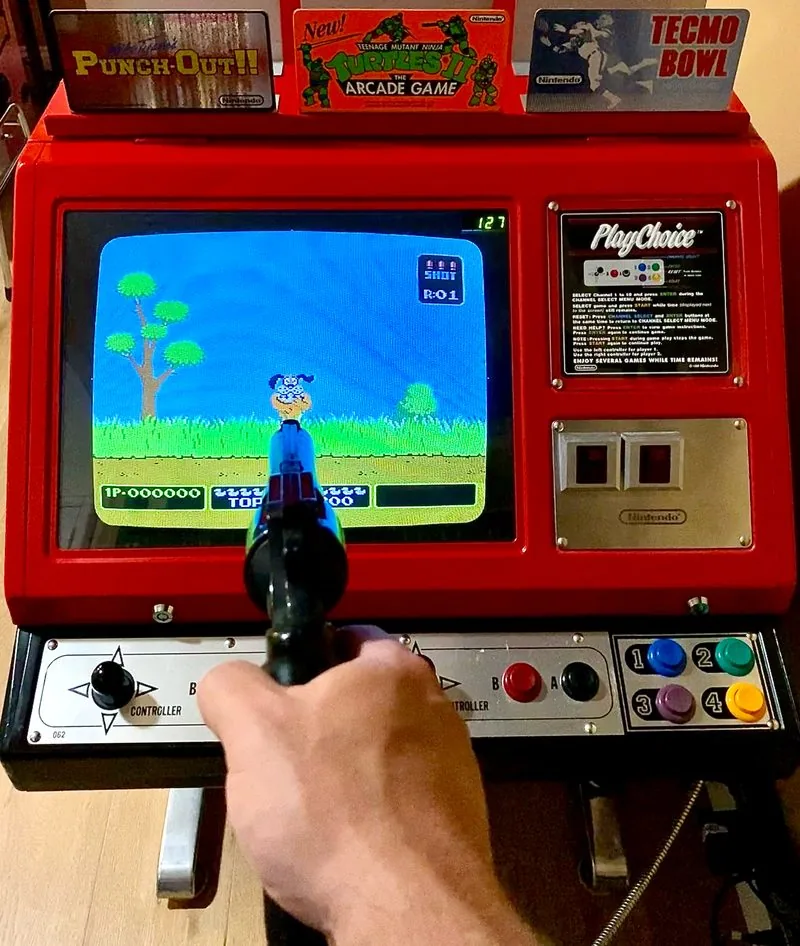 Playing VS. Duck Hunt on the Red Tent PlayChoice-10 side with the Zapper light gun in hand, and three PlayChoice-10 toppers on the canopy above